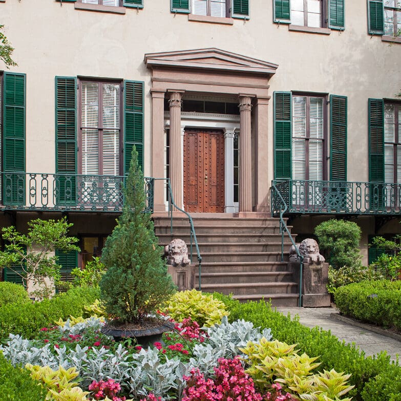 Exterior shot of Lowe House, with colorful front garden, bronze front door, and green shuttered windows