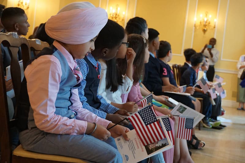 Children sit in a line, holding small American flags and brochures that read 