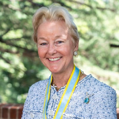 Headshot of Edith Stickney, a blonde woman in a blue and white button up jacket and a blue/gold medallion