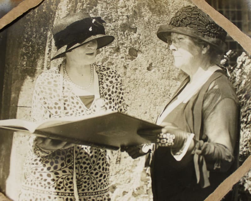 Black and white photo of two women in fancy hats and dress clothes holding a giant book