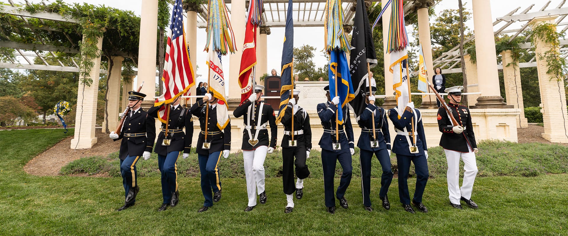 Line of military personnel marching down a grassy hill and holding different flags